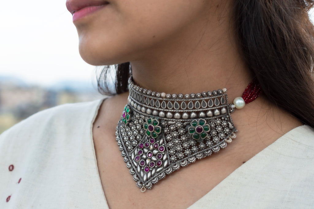 Close-up of a woman wearing an ornate silver necklace with gemstones.