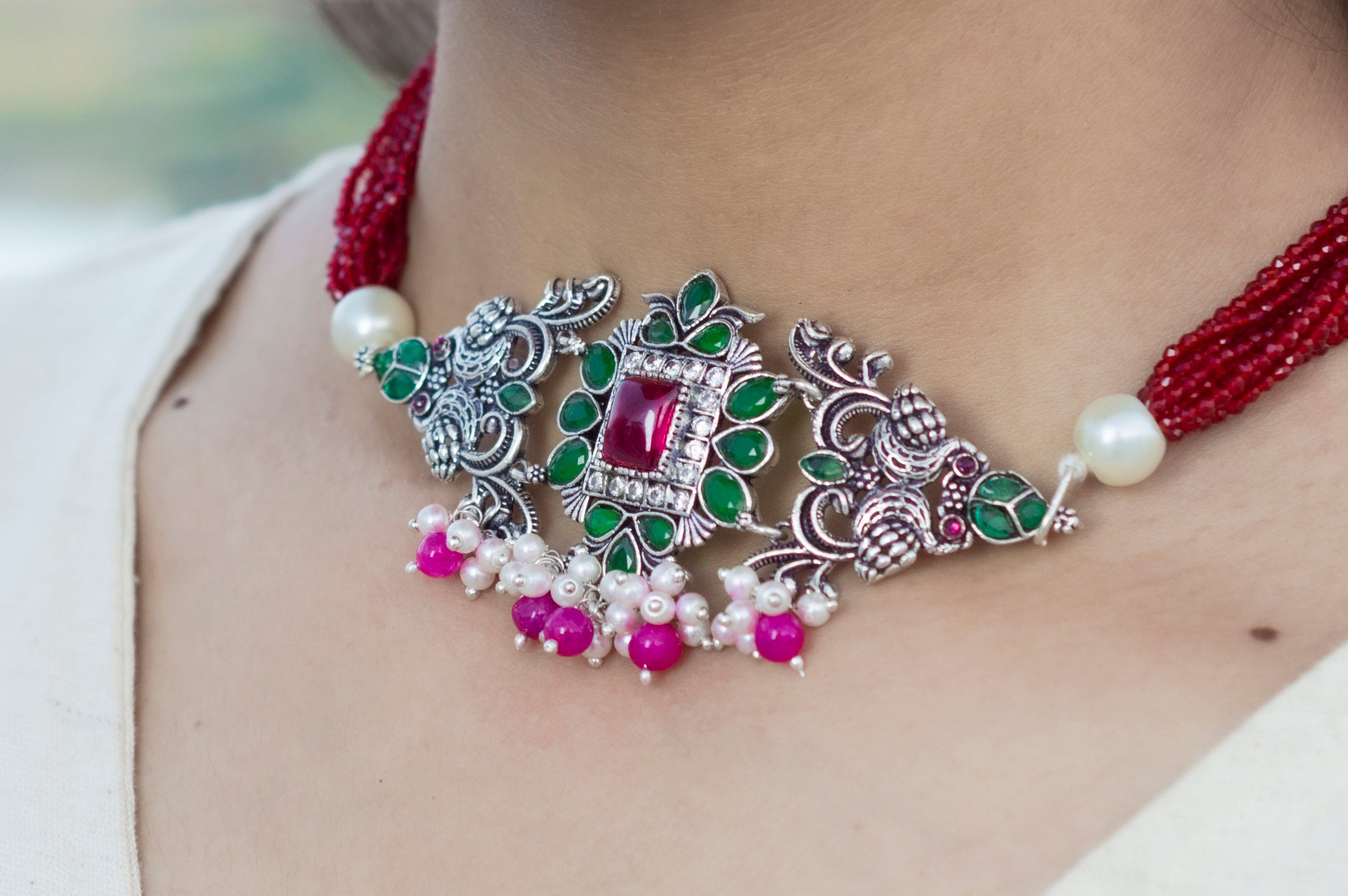Close-up of a woman wearing a decorative necklace with red, green, and pink stones.